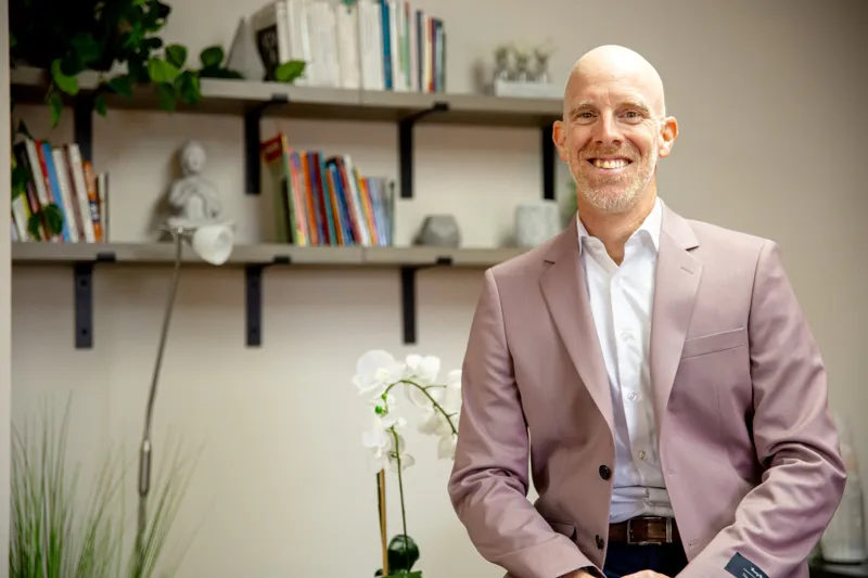 Éric Marchesseault souriant devant la bibliothèque de son bureau